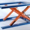 Sini-oranssi Edmo Lift -yksisaksiset matalat C-sarjan nostopöydät saksinostin valkoisella pohjalla.