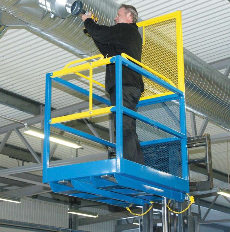Worker in a blue and yellow forklift work platform beside overhead ductwork